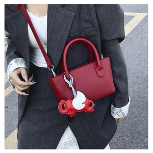 Detail of red litchi texture handbag with flying elephant charm on a grey suit