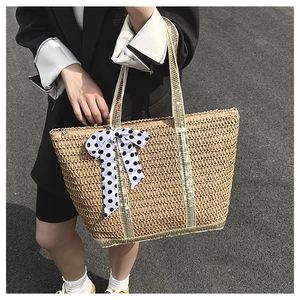 Détail du sac cabas en paille tissé avec anses dorées et un ruban à pois élégant