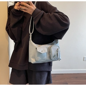 Detail view of light blue shoulder bag with metallic pockets on casual textured outfit
