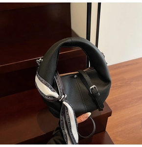 Detail der schwarzen Handtasche aus Leder mit Litschimuster und dekorativem Seidenschal