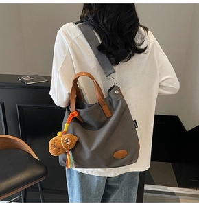 Detail of grey canvas tote bag featuring brown leather handles and a plush bear charm