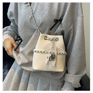 Close-up of cream bucket bag with lychee leather, pearl bow charm, and chain strap