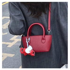 Detail of red lychee leather bucket bag with cute elephant charm on a casual outfit