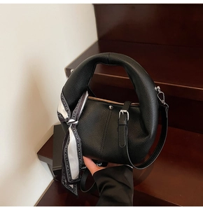 Detail einer schwarzen Handtasche aus Narbenleder mit elegantem gestreiftem Seidenschal