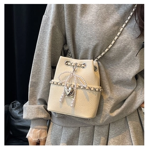 Detail of cream bucket bag featuring lychee texture with pearl bow and heart charm