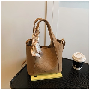 Close-up of beige leather bucket bag with silk scarf on a wooden table setting