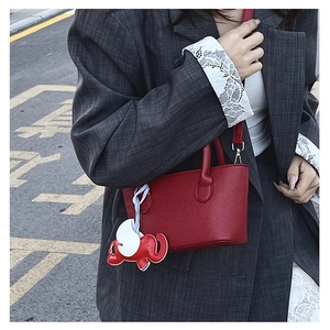 Detail of red litchi leather mini bucket bag with a cute elephant charm on a model