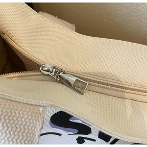 Detail shot of the silver metal zipper and purple letter print on the cream canvas tote bag