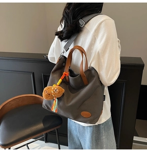 Detail of dark grey canvas tote with brown leather handles and plush bear charm