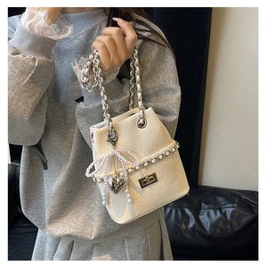 Detail of white bucket bag with pearl bow, heart pendant, and chain shoulder strap