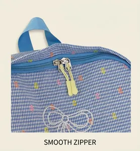 Close-up of smooth dual-zipper closure and cute embroidered bow on blue checkered school bag
