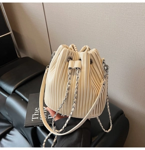Detailed view of cream pleated bucket bag with silver chain drawstring and leather strap