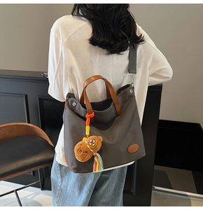 Detail of dark grey canvas tote with leather handles, shoulder strap and bear charm