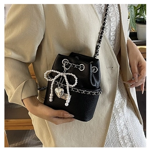Detail of black pebbled leather bucket bag with pearl bow and silver heart pendant charm