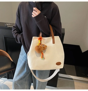 Detail of off-white canvas tote bag featuring brown leather trim and a cute teddy bear charm