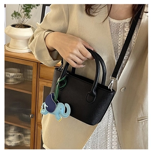 Detail of black lychee texture mini bucket bag with blue elephant charm and slim strap