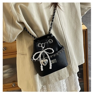 Detail of black quilted bucket bag with pearl bow and silver heart charm decoration