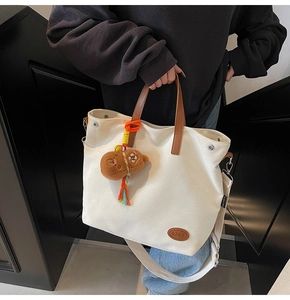 Detail of canvas tote bag with leather handles and a cute brown plush bear charm