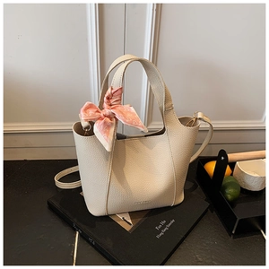 Detail of a beige lychee grain leather bucket bag with pink heart scarf and long strap