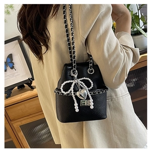 Close-up of black leather bucket bag with pearl bow, heart charm and chain strap