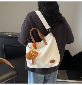 Detail of white canvas tote bag with brown leather handles and cute bear charm pendant