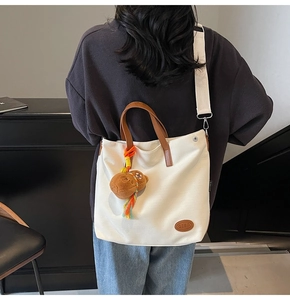 Detail of cream canvas tote with leather straps and cute brown bear charm accessory