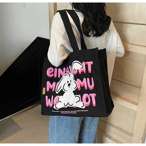 Detail of a large black canvas tote bag featuring a cartoon rabbit and artistic letter print
