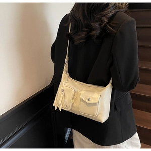 Detail of cream shoulder bag with dual functional pockets and adjustable strap shown on model