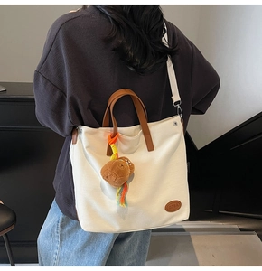 Detail of white canvas tote bag with brown leather handles and cute bear charm pendant
