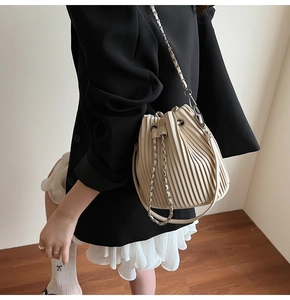 Detailed view of beige pleated bucket bag with chain strap worn with a black blazer