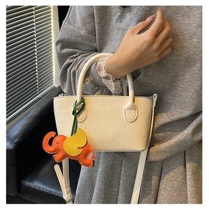 Detail of off-white lychee texture bucket bag with cute elephant charm and strap