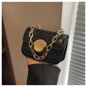 Close-up of black crocodile pattern leather bag with gold chain and round metal buckle