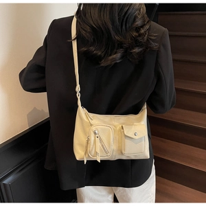 Detail of cream hobo bag featuring twin front pockets and polished hardware detail