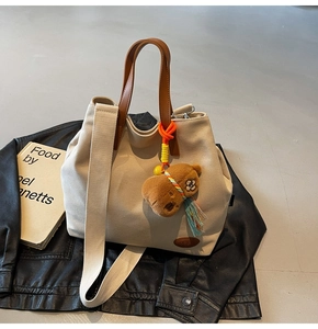 Detailed view of beige canvas tote with brown leather handles and plush bear charm
