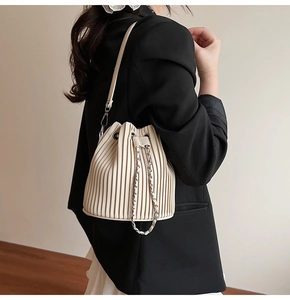 Detail of off-white pleated bucket bag with silver chain and thin strap on a shoulder