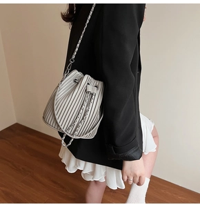 Close-up of off-white pleated bucket bag featuring metallic chain strap on model