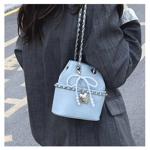 Detail of light blue bucket bag with silver chain and pearl bow on a grey blazer