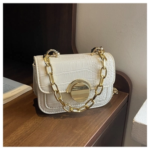 Close-up of beige crocodile pattern handbag with chunky gold chain and metal buckle detail