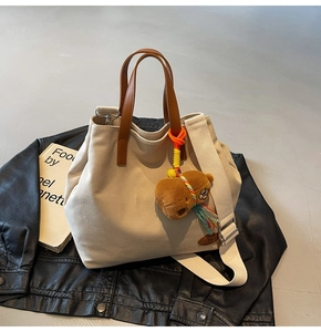 Detail of canvas tote bag with brown leather handles and a cute bear charm accessory