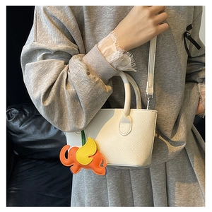 Close-up of white lychee pattern leather bucket bag with cute elephant charm accessory