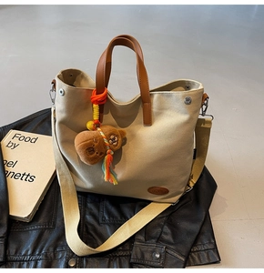 Detail of beige canvas tote bag with brown leather handles and plush bear charm accessory