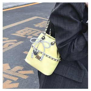 Detail of yellow quilted bucket bag with pearl bow and silver chain strap on model