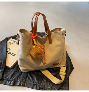 Beige canvas tote bag featuring brown leather handles and a cute plush bear charm