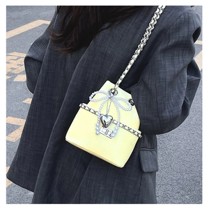 Detail of yellow bucket bag with lychee texture, pearl bow and silver heart charm