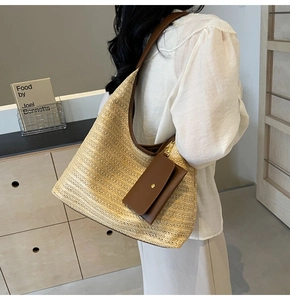 Detail view of woven straw tote bag with brown leather handles and small hanging pouch