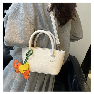 Detail of white lychee leather bucket bag with colorful elephant charm and slim shoulder strap