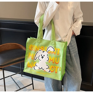 Close-up of light green canvas tote bag featuring a cute white cartoon rabbit and art text