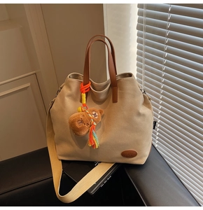 Detail of canvas tote bag featuring brown bear plush charm and rainbow tassel decor