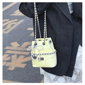 Detail of light yellow bucket bag with lychee grain texture and pearl bow decoration