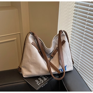Detail of canvas tote bag with brown leather straps and blue embroidery on black sofa